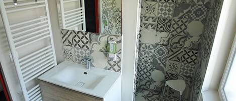 A bathroom with a white sink, mirror, towel rack, and patterned shower tiles.