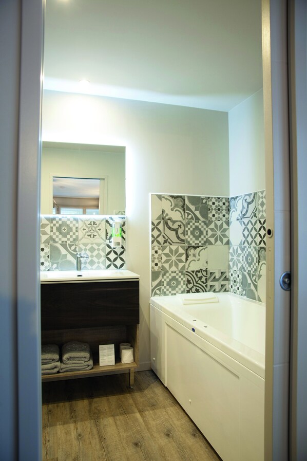 A bathroom with a white sink, a mirror, a shower with patterned tiles, and a shelf with towels. - Les Béthunoises Béthune Centre (Béthune)