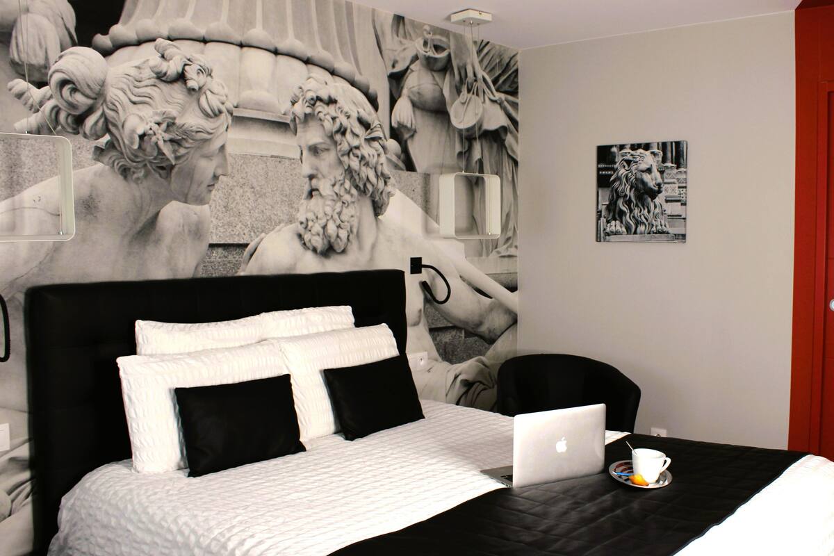 Un dormitorio con cama, laptop, taza y un mural en la pared.