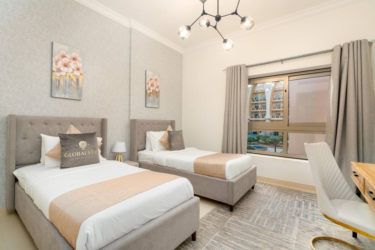 A hotel room with two beds, a sofa, a desk, and a large window with a view.