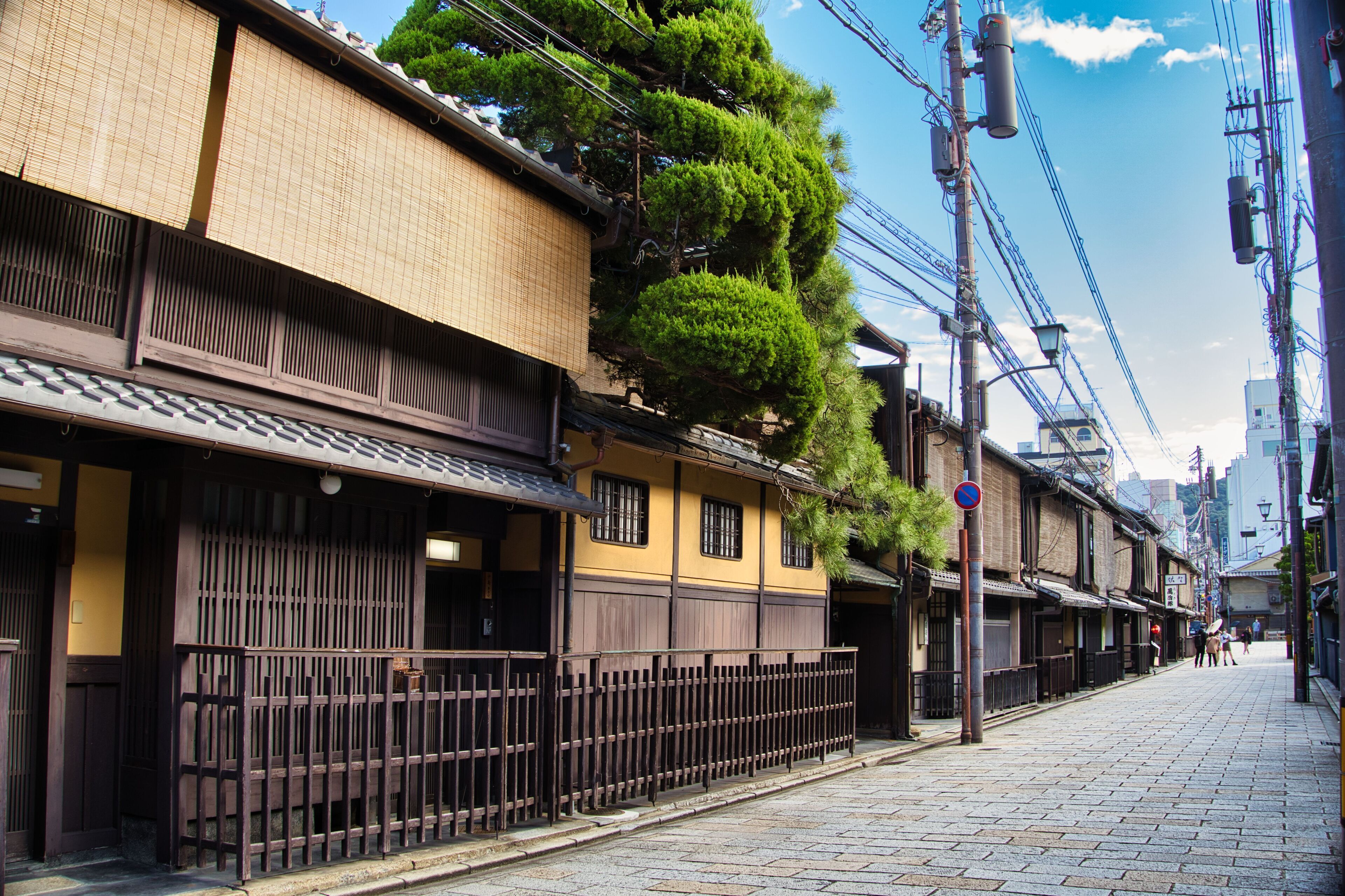 A traditional Japanese street with wooden buildings, a clear sky, and a pedestrian walkway.