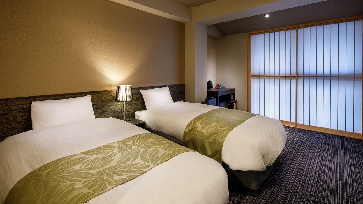 A hotel room with two beds, a nightstand, a lamp, and a sliding shoji screen.