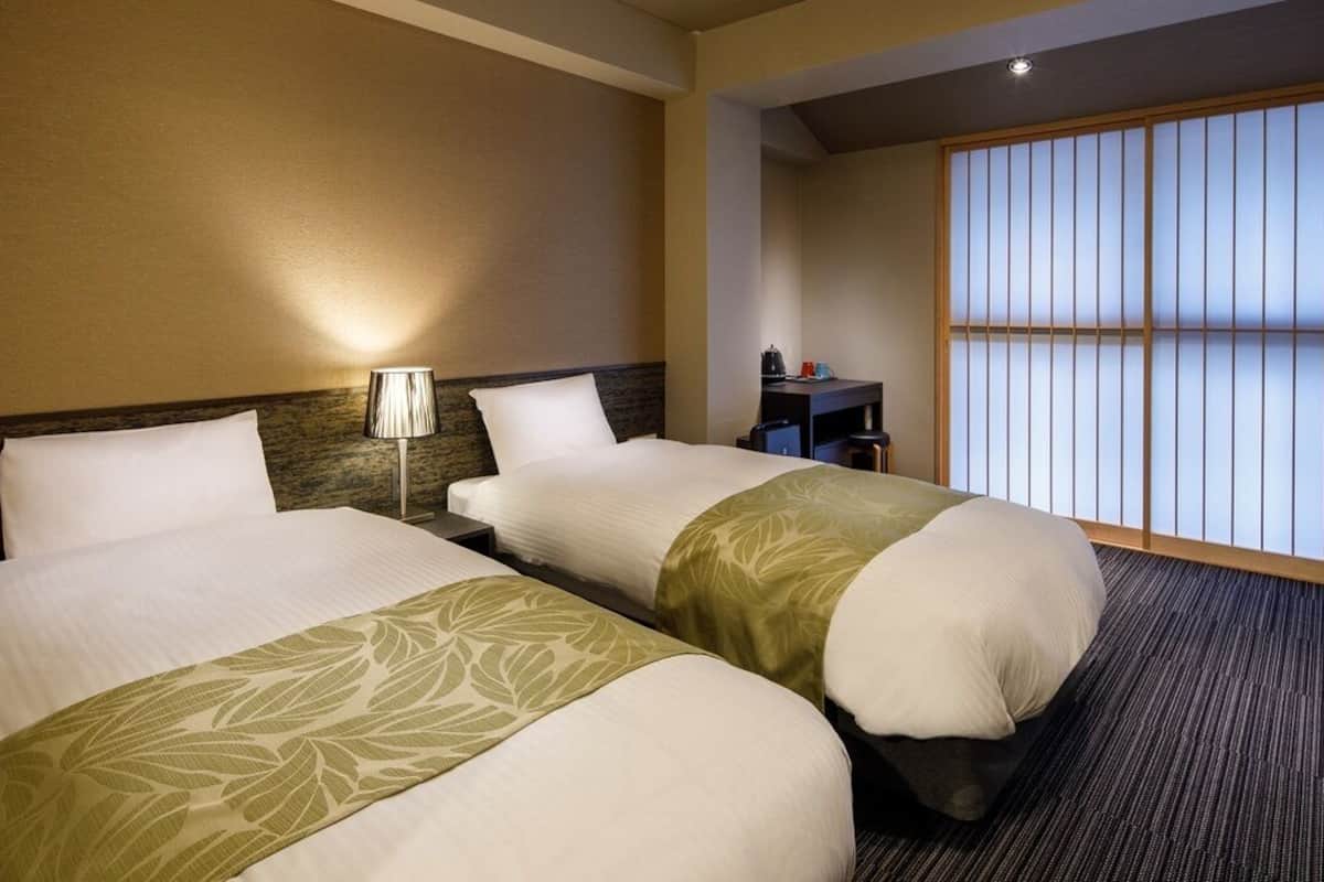 Ein Hotelzimmer mit zwei Betten, einem Nachttisch, einer Lampe und einem verschiebbaren Shoji-Bildschirm.