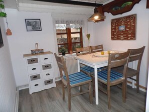 Un comedor con una mesa blanca, sillas a rayas azules, sillas de madera, un armario blanco y una lámpara colgante.