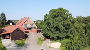 A large two-story building with a sloped roof, a garage, and a large tree in the foreground. - Ferienwohnung Obsthofterrasse - Obsthofterrasse (Drochtersen)