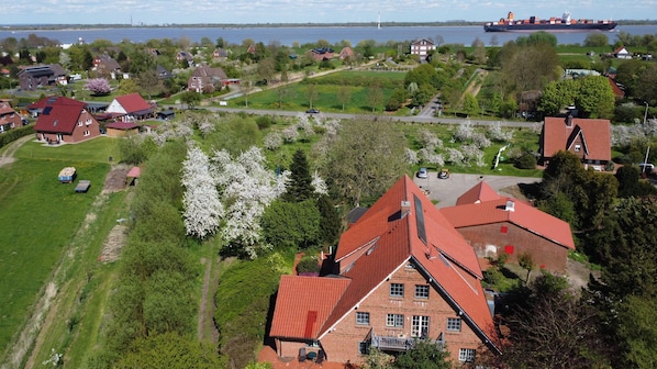 A residential area with houses, a large body of water, and a cargo ship in the distance. - Ferienwohnung Obsthofterrasse - Obsthofterrasse (Drochtersen)