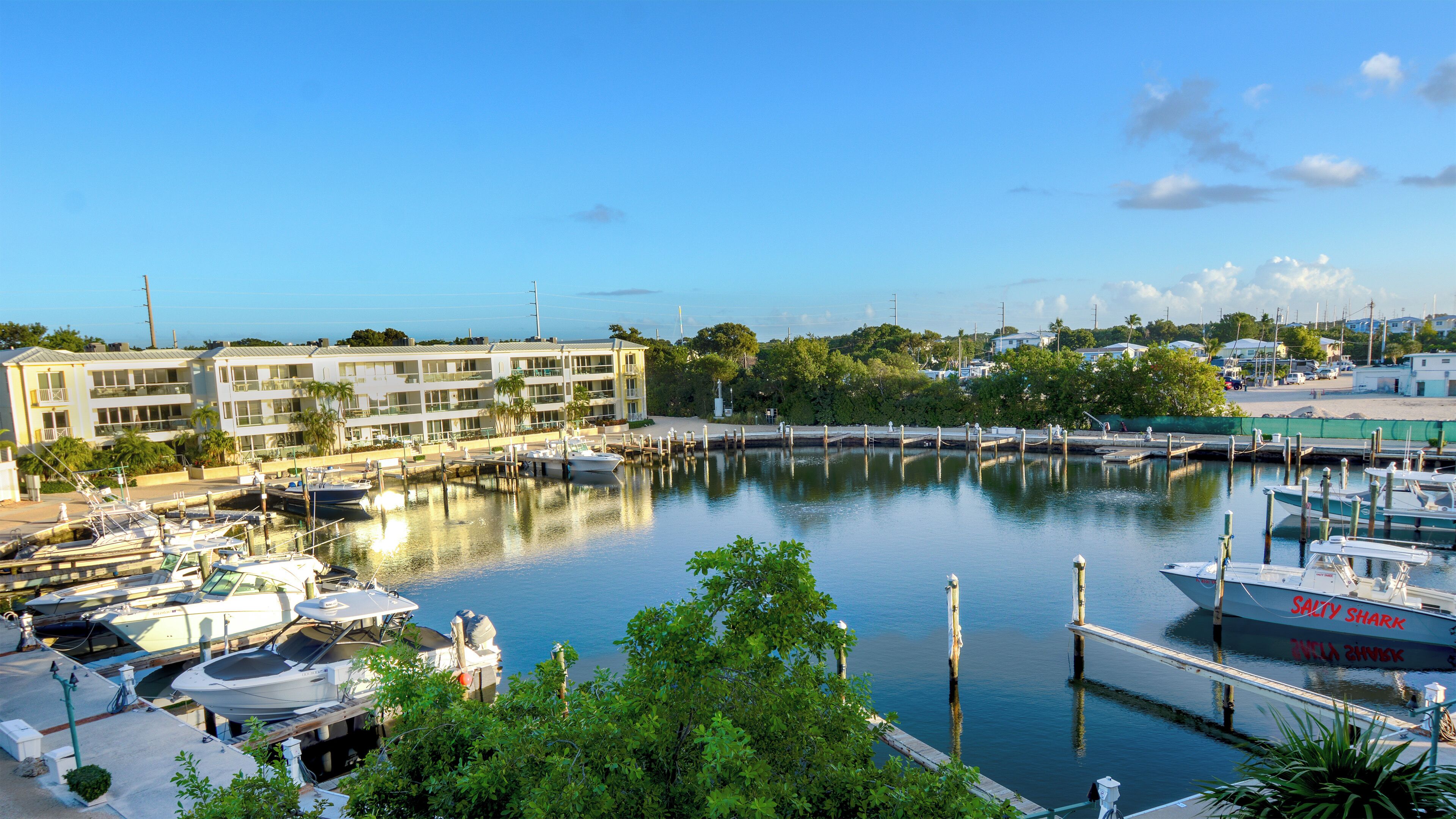 A marina with boats docked, a building with multiple floors, and a clear sky.