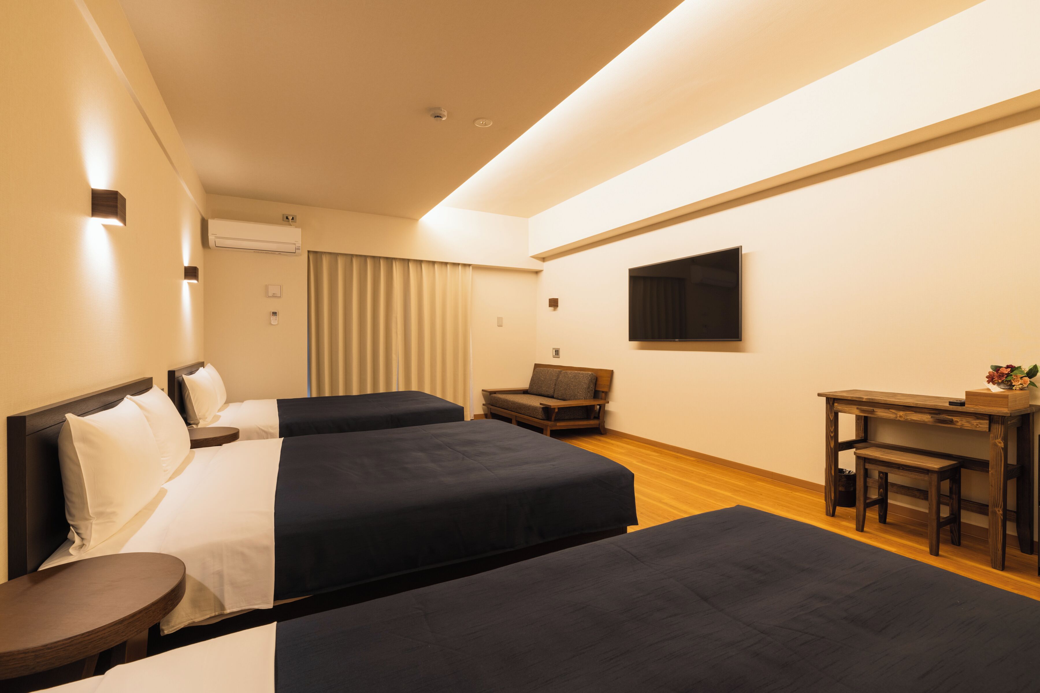 A hotel room with two beds, a desk, a chair, a TV, and a window with curtains.