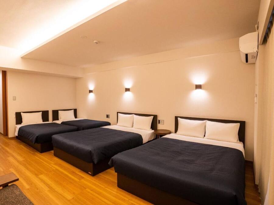 Una habitación de hotel con tres camas individuales, suelo de madera y luces fijadas a la pared.