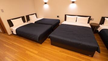 Habitación de hotel con tres camas individuales y una cama grande, todas con cabeceros negros y ropa de cama blanca.