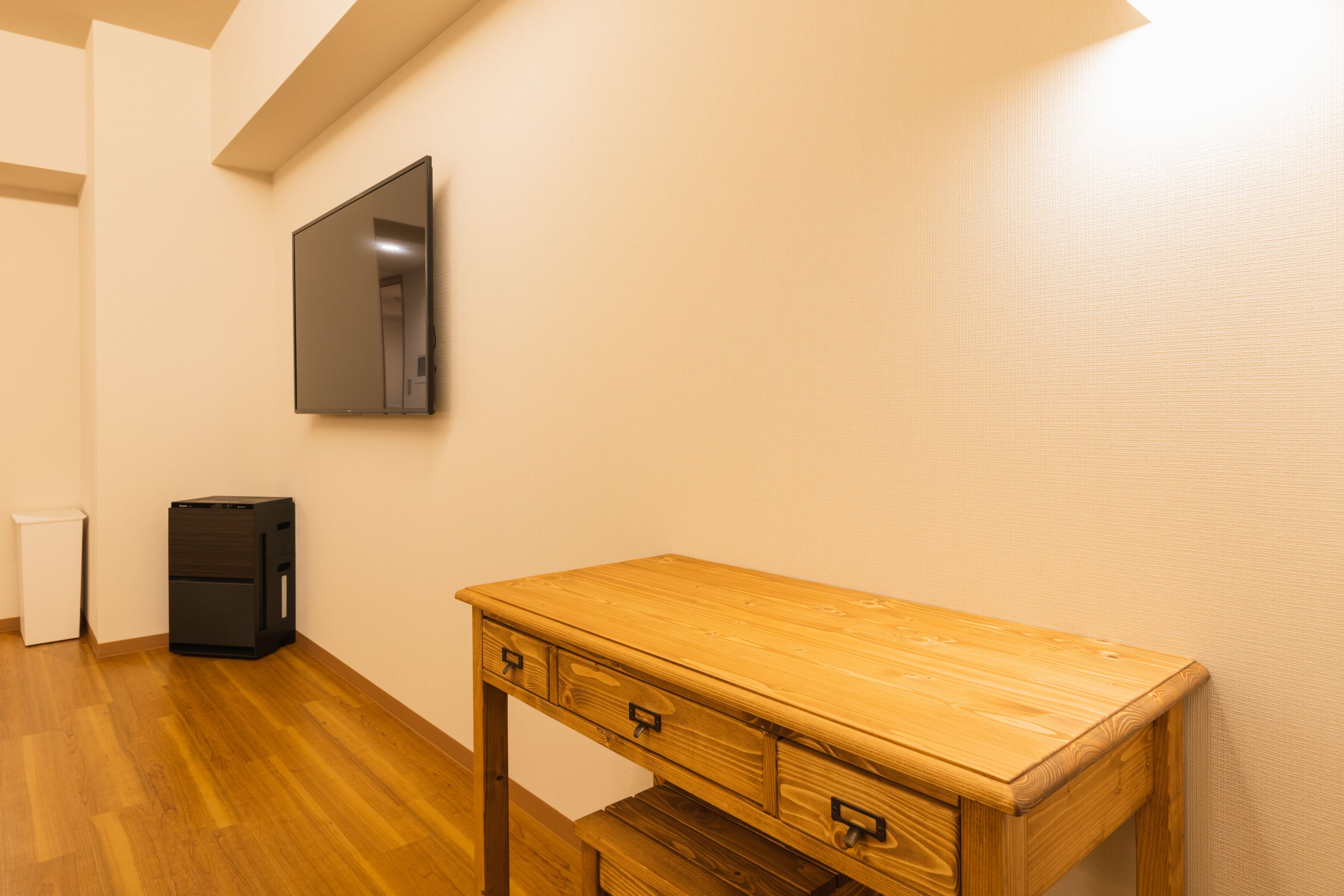 Une pièce avec un bureau en bois, un classeur noir et une poubelle blanche.