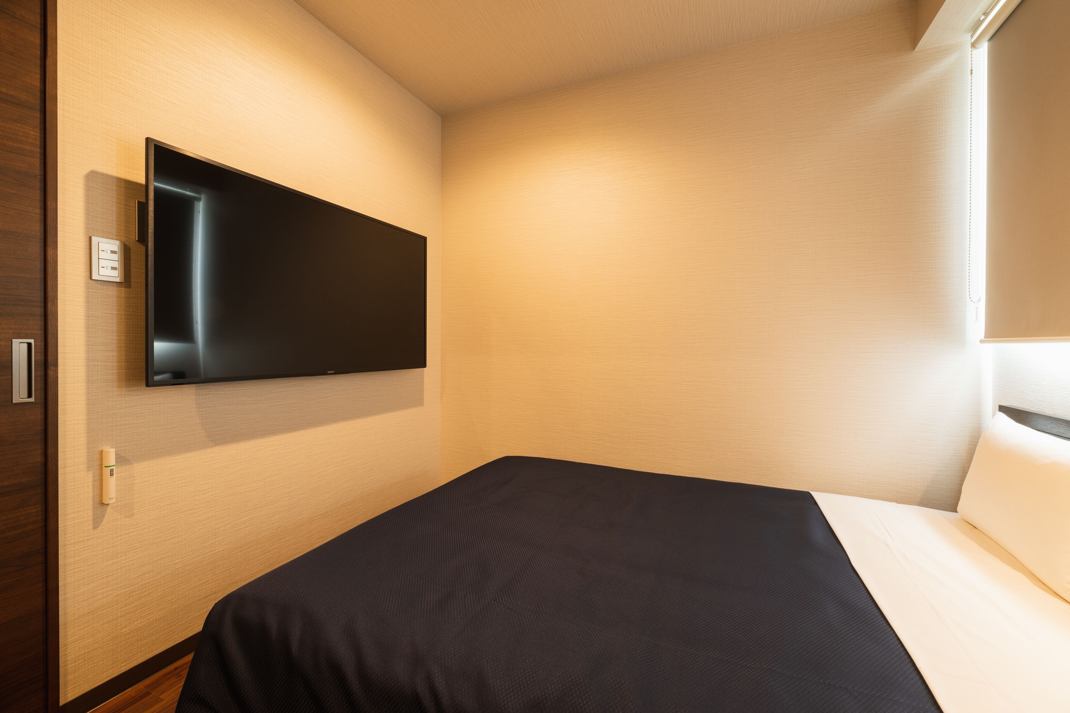 A modern hotel room with a flat-screen TV mounted on the wall, a neatly made bed, and a wooden floor.