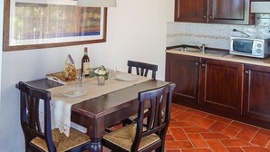A dining area with a wooden table, chairs, a framed picture, a microwave, and a tiled backsplash. - Casa Ruta A: A characteristic and welcoming apartment surrounded by the greenery, with Free WI-FI. (Monterotondo marittimo)