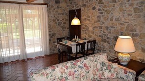 A cozy room with a stone wall, a wooden ceiling, a dining table with chairs, a floral sofa, and a table lamp. - Casa Ruta D: A characteristic and welcoming apartment surrounded by the greenery, with Free WI-FI. (Monterotondo marittimo)
