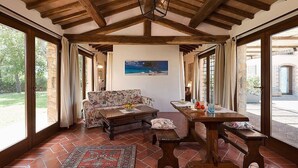 A spacious room with a wooden ceiling, a large window, a sofa, a table, and a rug.