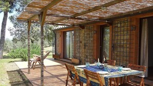 Een buitenmeubilairgedeelte met een houten tafel en stoelen, overdekt door een pergola.