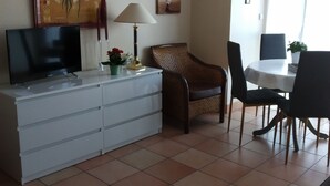 A living room with a TV, a lamp, a dining table, and chairs. - BEAUTIFUL T2 APARTMENT with secure parking, 8-minute walk to beach, ports, center,  (LES SABLES D'OLONNE)