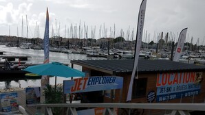 A marina with boats docked, a wooden structure with a sign for 'JET EXPLORER' and 'LOCATION', and a cloudy sky. - BEAUTIFUL T2 APARTMENT with secure parking, 8-minute walk to beach, ports, center,  (LES SABLES D'OLONNE)