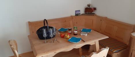 Un banc en bois avec une table devant, un panier, des verres à vin, des pommes et des pots de confiture.