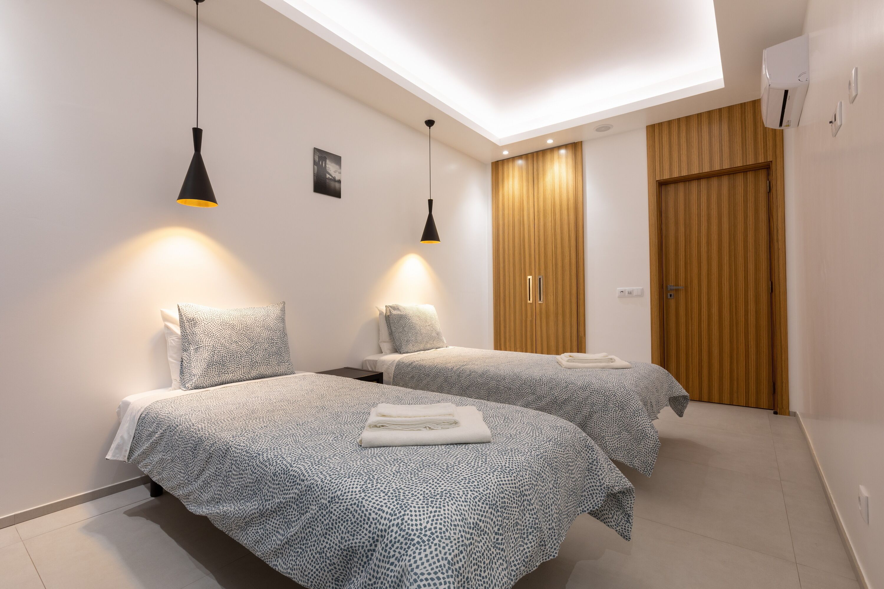 A modern bedroom with two beds, a skylight, and a wooden wardrobe.