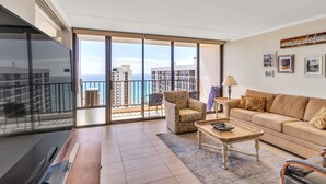 A spacious living room with a large sliding glass door leading to a balcony with a city view.