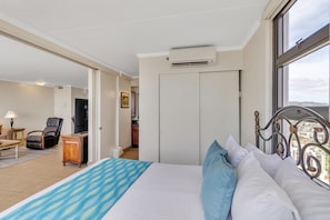 A hotel room with a bed, a desk, a chair, and a view of the city through a window.