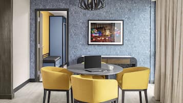 A modern dining area with a round table, four yellow chairs, a laptop, and a framed picture on the wall.