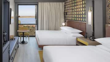 A hotel room with two beds, a dining table, a view of the water, and a wall with a number pattern.