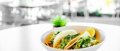 Un plato de tacos sobre una mesa blanca con un fondo desenfocado.