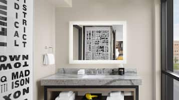 A modern bathroom with a marble sink, a large mirror, and a view of the city through a window.