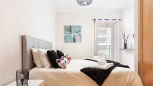A neatly made bed with a white duvet and black throw blanket, a bedside table with a black lamp, and a wall-mounted artwork.