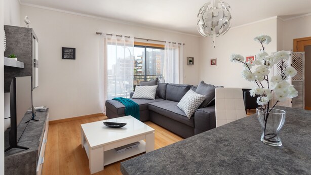 A modern living room with a grey sofa, white coffee table, and a glass vase with flowers.