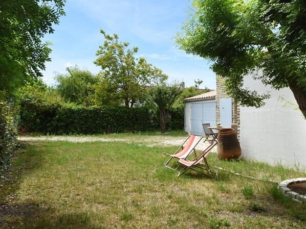A grassy backyard with a small garden area, a wooden chair, and a large pot. - Charming Home Near Village Center with Garden & Modern Amenities (Les Portes-en-Ré)