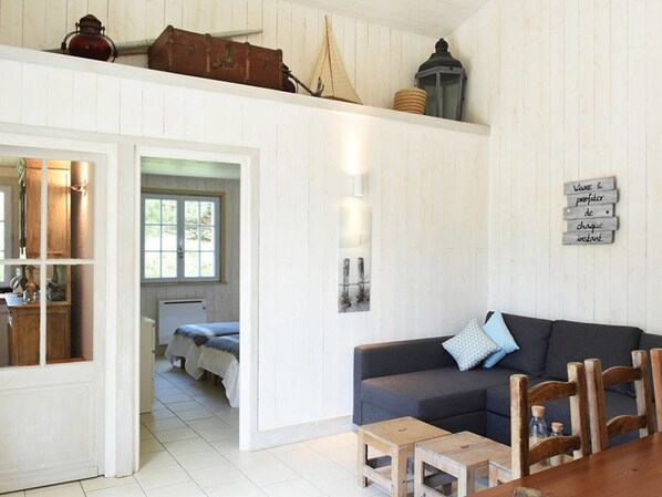 A cozy living room with a dark sofa, wooden coffee table, and a dining table. A wooden cabinet and a window with curtains are visible.