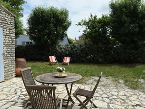 A stone patio with a round table and four chairs, surrounded by greenery and a stone wall.