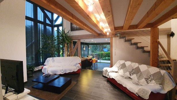 Un salon spacieux doté d’une grande fenêtre, de poutres en bois, d’une cheminée et d’un escalier.