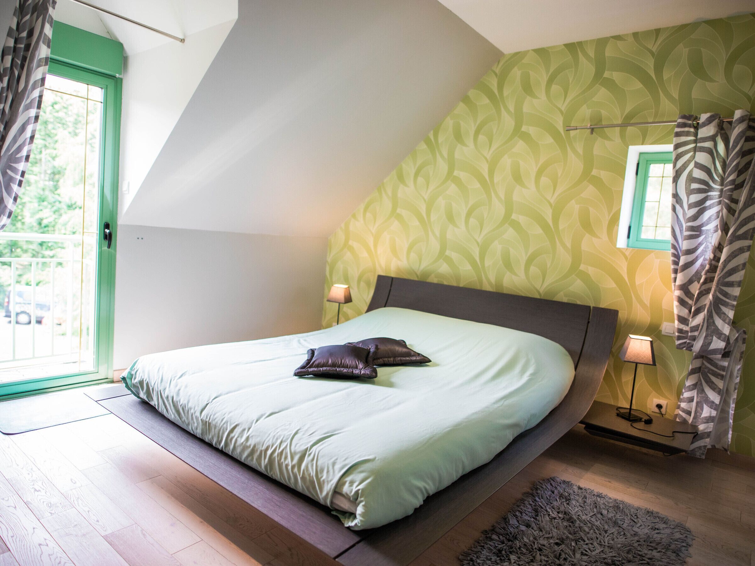 A bedroom with a bed, pillows, a lamp, a rug, and a window with curtains.
