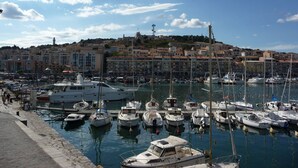 Ein Yachthafen mit verschiedenen Schiffen, eine Uferpromenade und eine Stadt am Hang im Hintergrund.