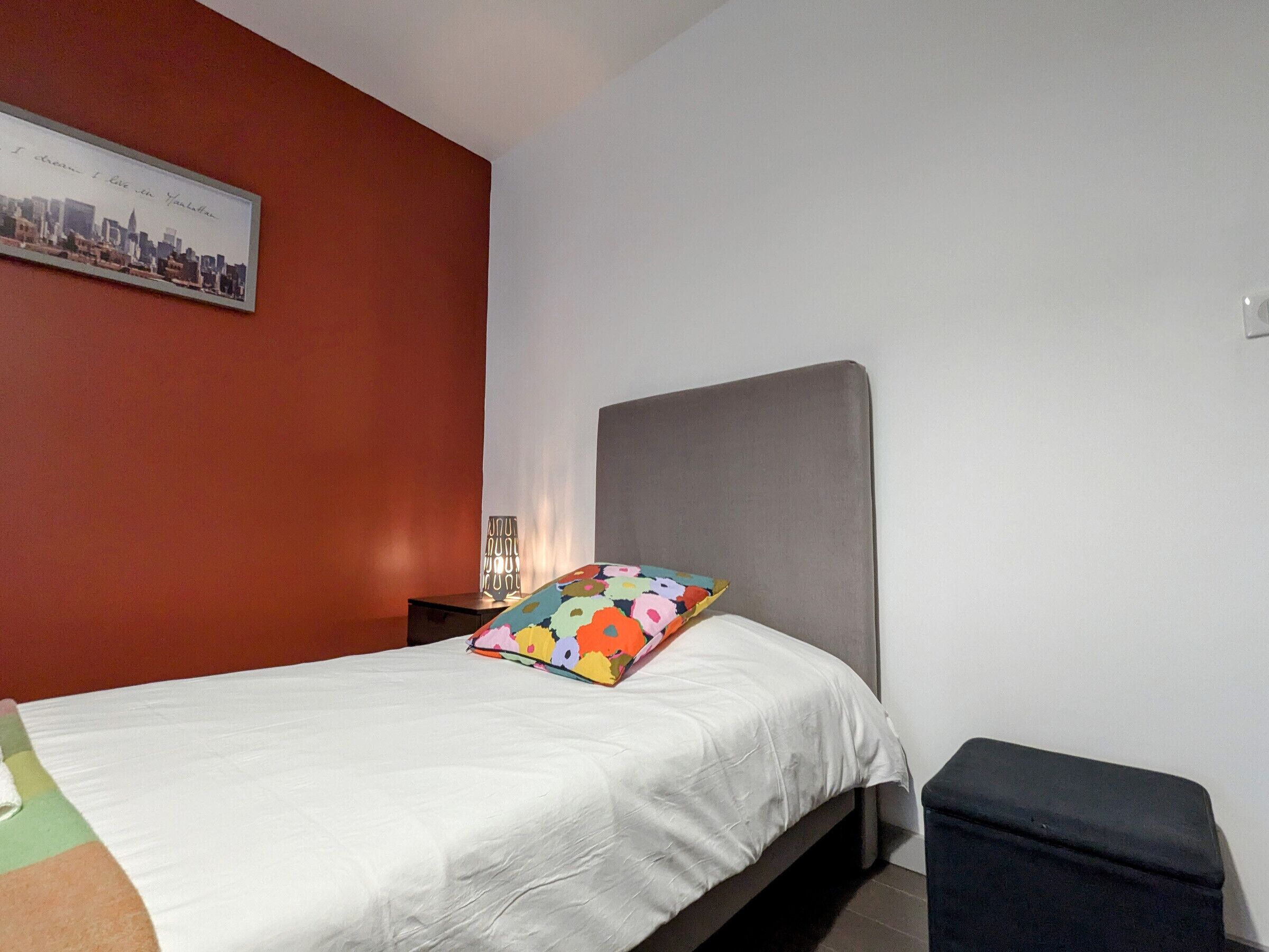 A bedroom with a bed, a pillow, a nightstand, and a wall with a framed picture.