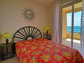Relax in this inviting room with a large bed, decorative mirror, and sliding glass door leading to a balcony with a sea view.