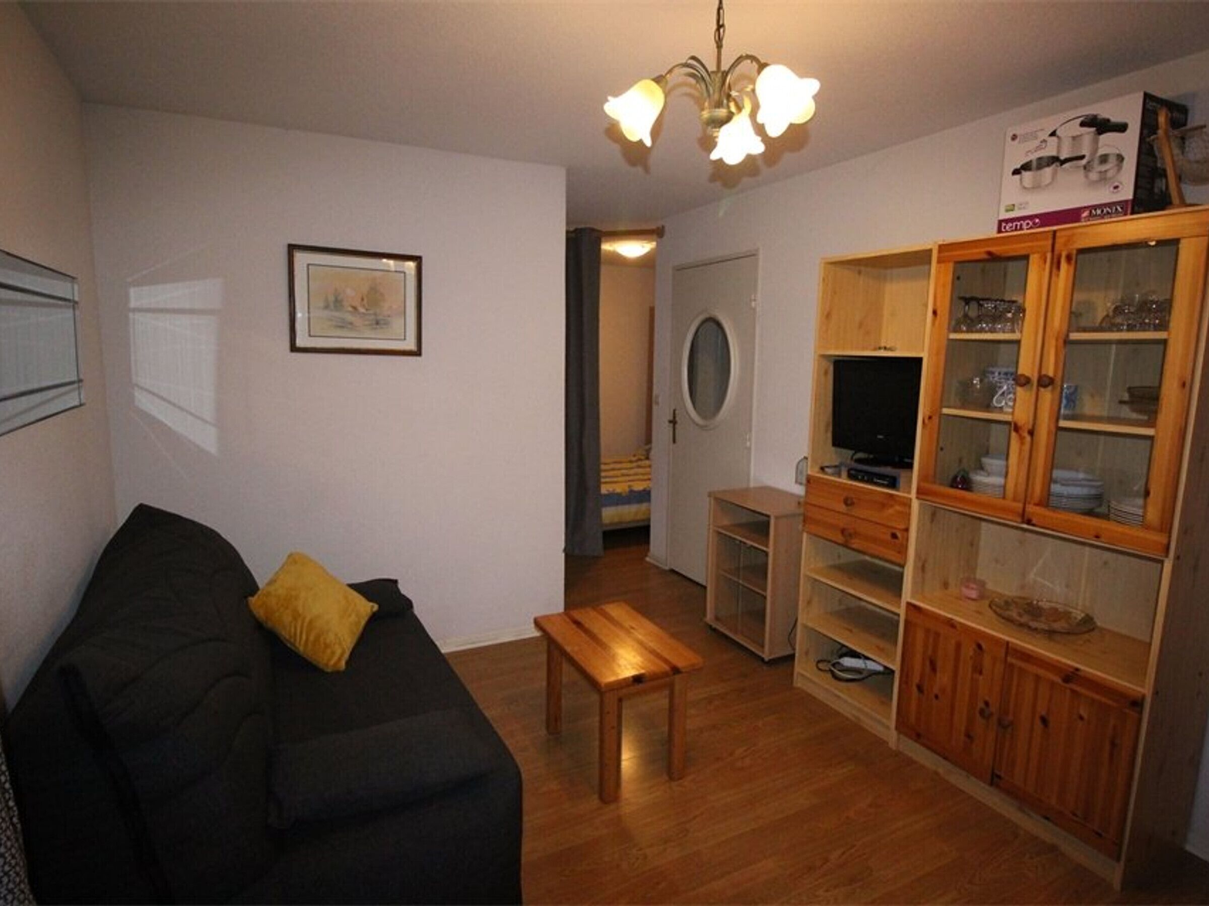 A living room with a black sofa, a wooden bench, a TV stand, and a cabinet with glass doors.
