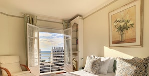 A room with a bed, a chair, a window with a view of buildings, and a painting on the wall. - N&J - BEACH COTTAGE TERRACE  - Very close sea (Niza)