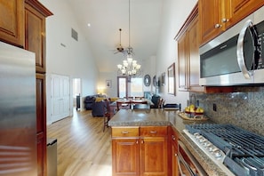 A spacious kitchen with wooden cabinets, a stainless steel refrigerator, a built-in microwave, and a granite countertop.