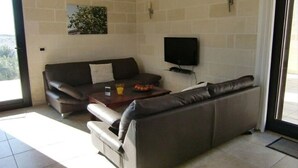 A living room with a sofa, a coffee table, and a flat-screen TV mounted on the wall. - VILLA AMICORUM House EAST, pool 10 x 4 m  (San Pietro in Bevagna)