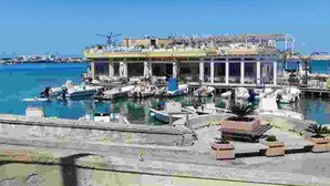 A waterfront building with multiple balconies, a dock with boats, and a clear blue sky. - VILLA AMICORUM House EAST, pool 10 x 4 m  (San Pietro in Bevagna)