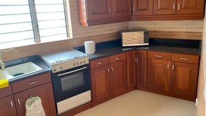 Cucina con mobili in legno, piano cottura, forno, microonde e una finestra con persiane.
