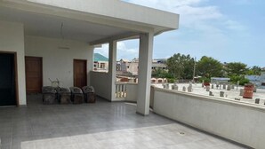 Un ampio balcone con pavimento piastrellato, qualche sedia e vista sugli edifici e il verde circostante.