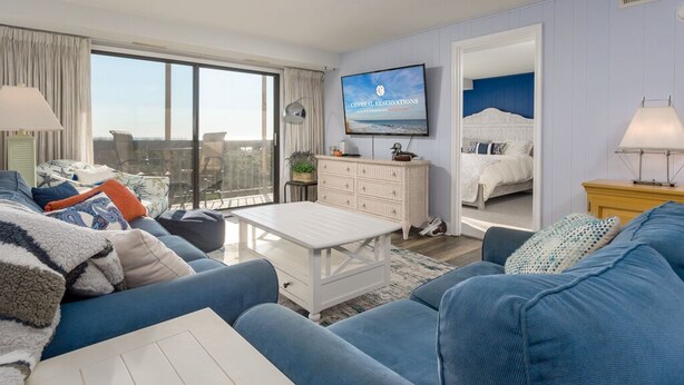 A modern living room with a large window, a television, a white coffee table, and a sofa. - Direct oceanfront in convenient mid town location (Ocean City)