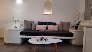 A modern living room with a sofa, a round coffee table, and a side table with a lamp. - Vitsentzos Suites (Santorini)