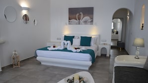 A modern hotel room with a large bed, a bedside table, a small table with decorative items, and a mirror. - Vitsentzos Suites (Santorini)